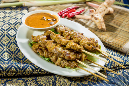 Thai-style grilled satay skewers served on lettuce with peanut sauce, surrounded by chili, lemongrass, and galangal.の写真素材