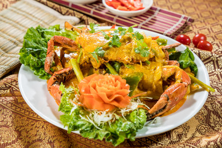 Thai-style crab coated in yellow curry sauce, garnished with cilantro, cabbage, and carrot flower on white plate.の写真素材