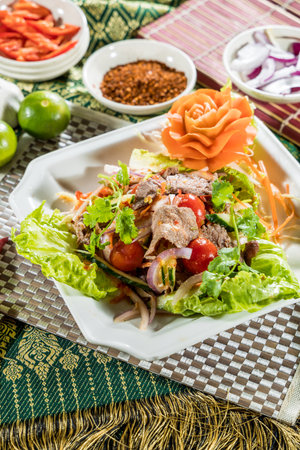 Thai-style beef salad with grilled beef, fresh vegetables, and chili garnish, served on a white plate.の写真素材