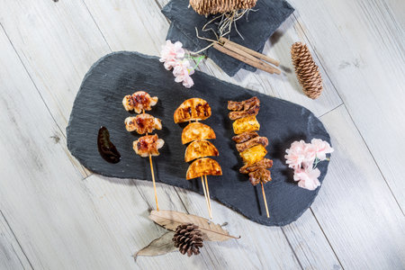 Three skewers with bacon, shrimp, dumpling or mushroom, and meat with pineapple, served with sauce and rustic decorations.の写真素材