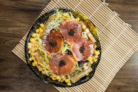 A salad bowl with cured meat slices topped with corn, greens, and shredded vegetables.の写真素材
