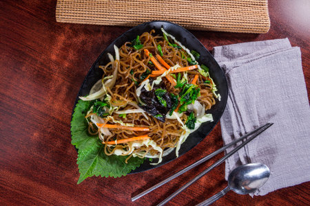 A plate of Korean stir-fried glass noodles with colorful vegetables like carrot, spinach, cabbage,...