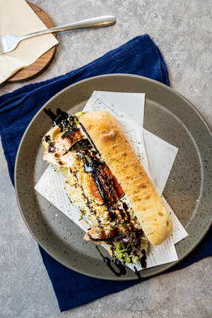 A plate with a grilled sandwich filled with vegetables and meat drizzled with dark sauce served on a blue cloth.の写真素材