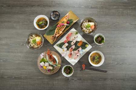A complete Japanese meal featuring assorted sushi, grilled prawns, udon noodles, and side dishes...