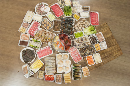A large spread of assorted hot pot ingredients including meat slices, seafood, vegetables, and mushrooms arranged around a pot of spicy broth.の写真素材