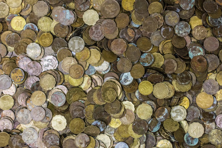 A large pile of assorted coins in various sizes and colors, some tarnished and old, representing a...