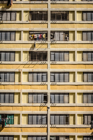 A multi-story residential building with metal grilles, laundry, and yellow-beige facade, showing...