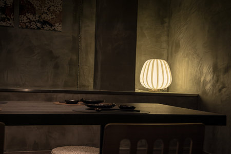 A dimly lit modern dining area with black dishes, floral wall art, and a glowing lamp, creating a...