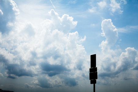 A silhouette of a tall road sign with three panels against a bright sky filled with cumulus clouds, creating dramatic contrast.の写真素材