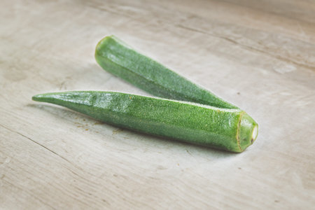 Two green okra pods with ridged texture and fuzzy surface, fresh vegetable.