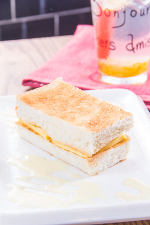 A close-up of toasted bread layered with cheese and drizzled with condensed milk on a white plate.