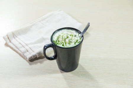 A black ceramic mug filled with creamy matcha latte topped with whipped cream and green tea powder...