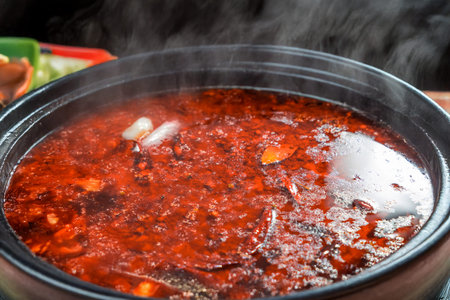 Close-up of a boiling pot of chili oil broth with dried peppers and spices.