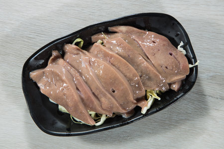 Raw pork liver slices arranged on a black plate with shredded cabbage garnish.