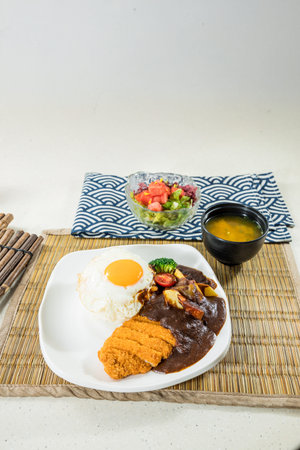 A plate of Japanese curry rice served with fried pork cutlet, sunny-side egg, and vegetables, hearty meal.の写真素材