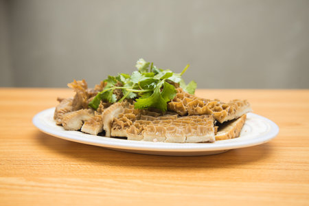 A white plate of sliced beef tripe garnished with fresh coriander leaves.
