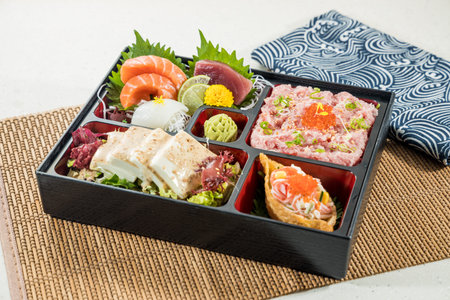 A black bento box filled with sashimi, tofu, and sushi garnished with vegetables.