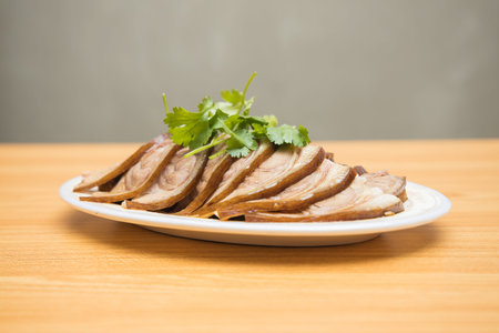 A white plate of sliced braised beef shank garnished with fresh coriander leaves.