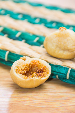A close-up of a dried fig split open showing seeds inside, placed on a green and beige woven mat.