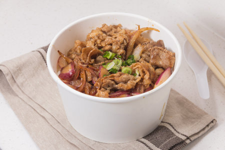 A white bowl filled with cooked beef slices mixed with onions and sauce, served hot and flavorful.