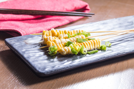 A black rectangular plate with four skewers of spiral-cut vegetables garnished with chopped green onions.の写真素材