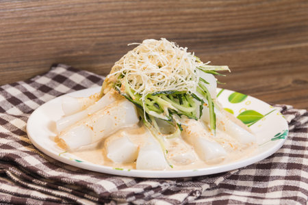 A white plate of rice rolls topped with shredded cucumber and crispy garnish, served with sesame...