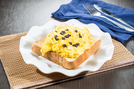 A white plate with scrambled eggs served on a slice of toast topped with black garnish.