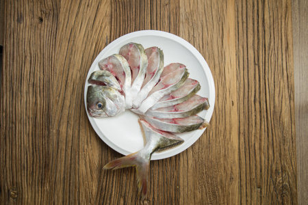Top down view of a whole fish arranged on a white plate with the head and tail intact. The body is...