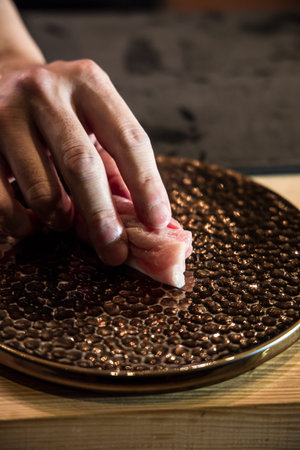 Close up of a chef hand placing a piece of fatty tuna nigiri onto a textured bronze plate on a...