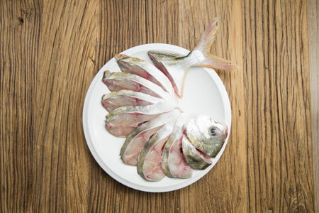 On a round white plate, a fish is expertly sliced and fanned while keeping the head and tail...
