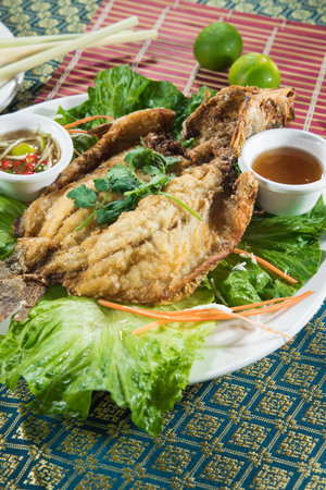 Portrait plate with a deep fried whole fish on leafy greens, served with two dipping sauces and...