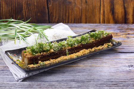 A long grilled eggplant topped with chopped green onions and crushed peanuts served on a black plate