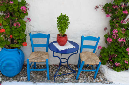 Traditional Blue Greek Restaurant Table and chairs against to white painted wall with flowers の写真素材