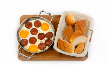 Fried eggs with sausage and bread on a wooden board isolated on white backgroundの素材