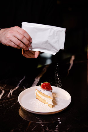 Chef sprinkling whipped cream on a piece of cake with strawberriesの素材