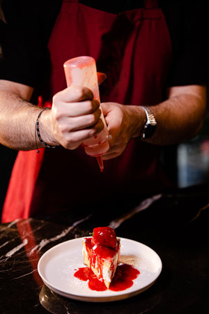 Chef decorating a cake with strawberry sauce on a black backgroundの素材