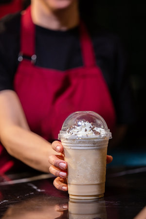 Close up of female barista holding ice coffee with whipped cream.の素材