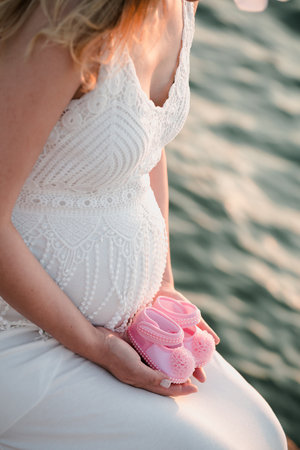 Pregnant woman with baby booties on the sea background.の素材