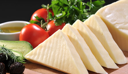 Sliced cheese on a cutting board with vegetables and olive oilの素材