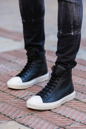 Close up of men's legs in black jeans and white sneakers.の素材