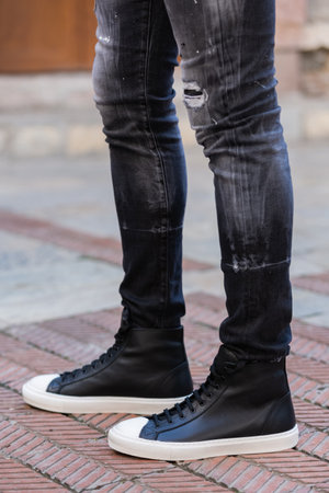 Close up of man's legs in black jeans and white sneakers.の素材