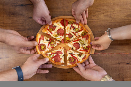 Top view of a group of people taking a slice of pizza from a wooden table