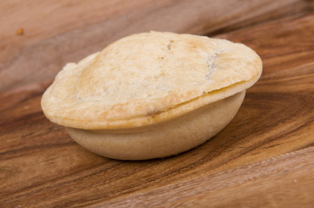 Uncooked australian meat pie on a wooden chopping board