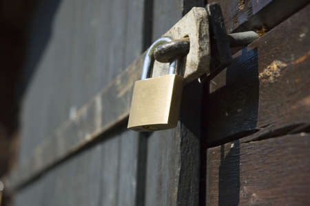 A yellow padlock securing a black wooden doorの写真素材