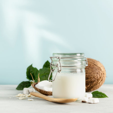 Coconut oil in jar with fresh coconut and tropical leaf shadow, square compositionの写真素材