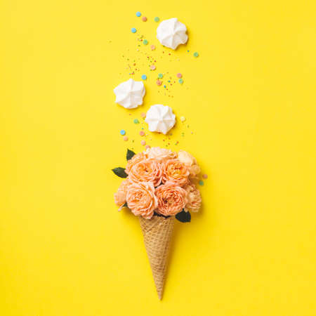 Ice cream cone with pink roses and merengues on yellow backgroundの写真素材