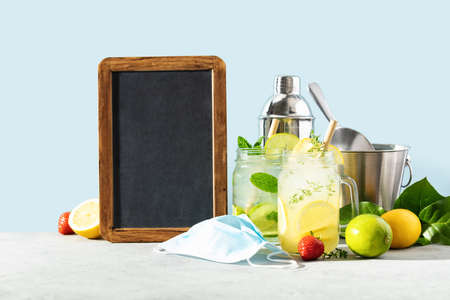 Fresh cocktails, ice bucket, medical mask and chalkboard on blue sky background. Bar, cafe, restaurants reopen after coronavirus. Quarantine is over conceptの写真素材