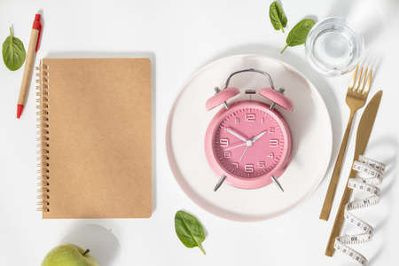 Composition with cutlery, measuring tape, blank paper notebook and alarm clock on color background. Diet concept, copy spaceの写真素材