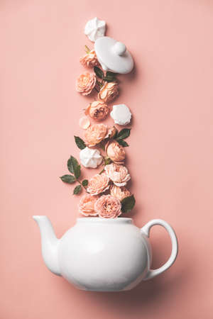 Creative layout made of whte tea pot with orange roses and merengues on pink backgroundの写真素材