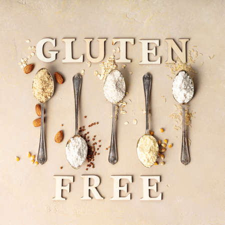 Metal spoons of various gluten free flour (almond flour, oatmeal flour, buckwheat flour, rice flour, corn flour) and gluten free lettering made of wooden letters, flat lay, top viewの写真素材